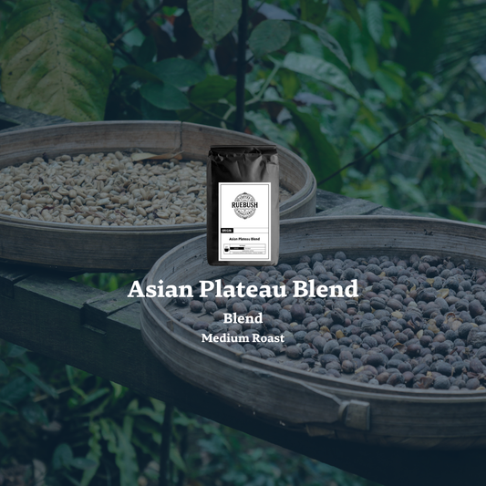 Coffee blend packaging labeled Asian Plateau Blend with coffee beans in wooden trays against a green leafy background