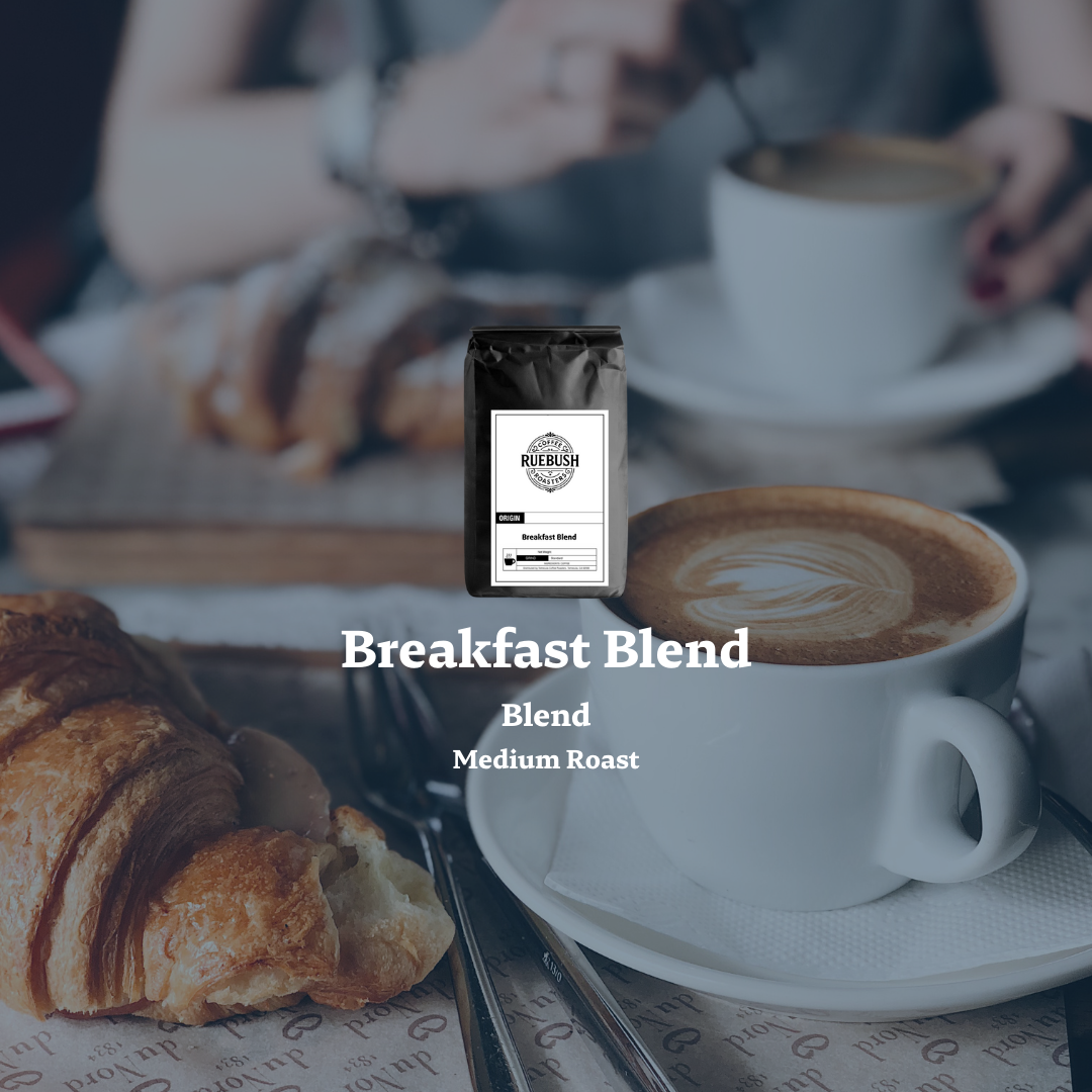 Cup of coffee with a croissant and a coffee bag labeled Breakfast Blend Medium Roast on a table
