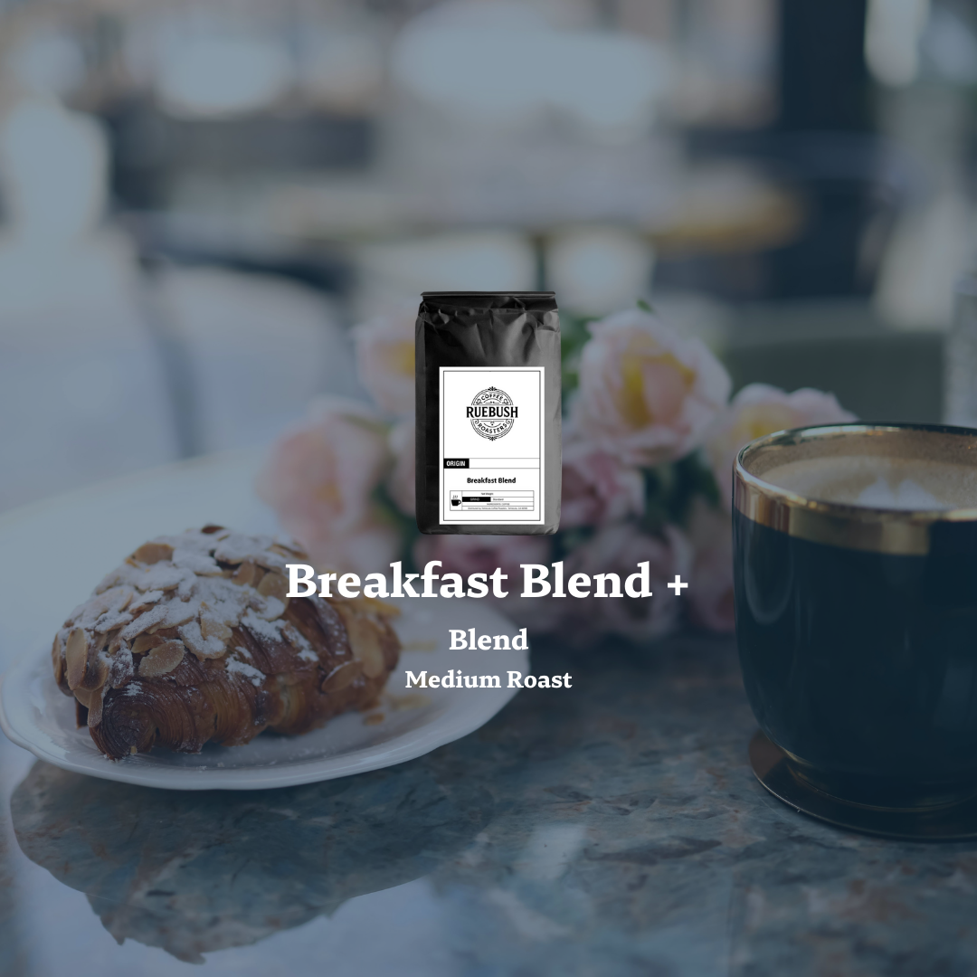 Coffee bag labeled Breakfast Blend + with a croissant and coffee cup on a blurred background