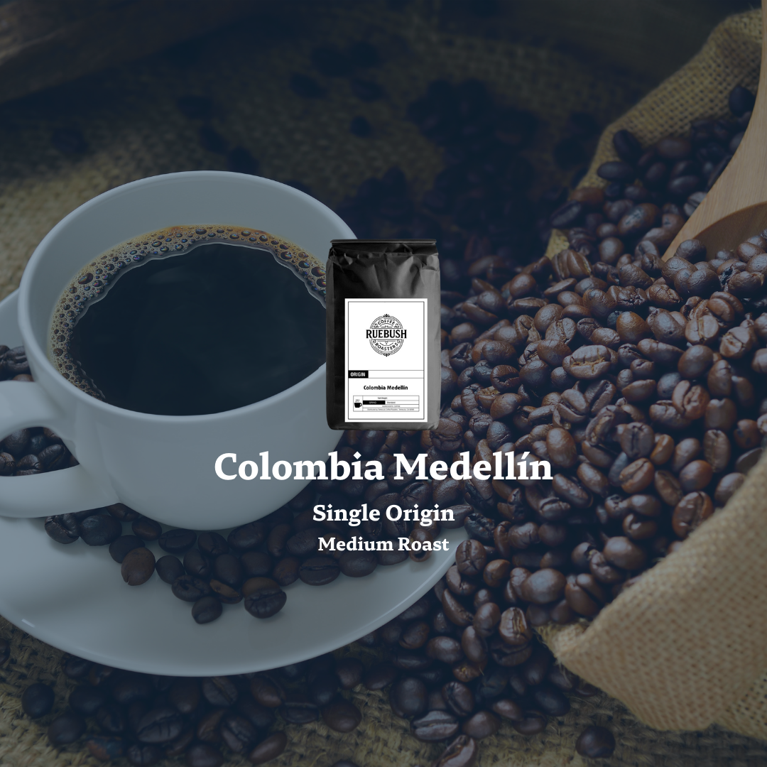 White cup of coffee with coffee beans and a wooden scoop on a dark background, featuring Colombia Medellín Single Origin Medium Roast text