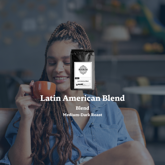 Woman holding a coffee cup with a Ruebush Coffee Roasters bag labeled Latin American Blend in a blurred cafe setting