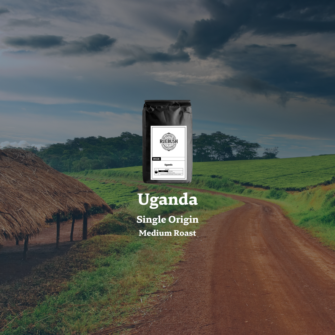 Coffee bag labeled Uganda Single Origin Medium Roast on a dirt road with a hut and green fields in the background.