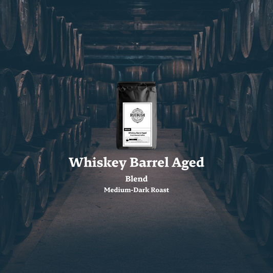 Coffee bag labeled Whiskey Barrel Aged Blend by Ruebush Coffee Roasters in a warehouse setting with barrels