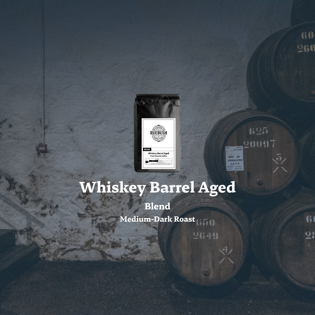 Coffee bag labeled Whiskey Barrel Aged Blend by Ruebush Coffee Roasters with stacked barrels in the background