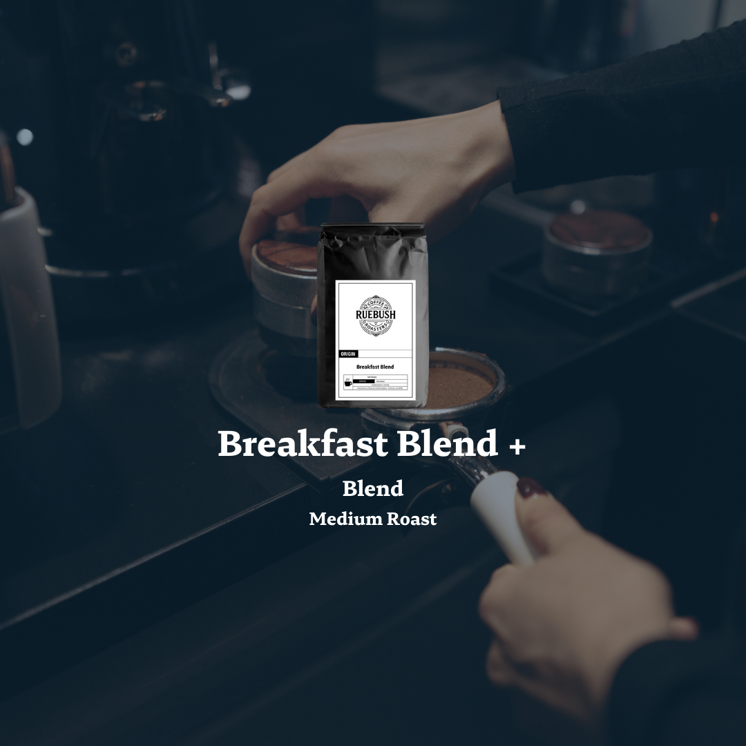 Person holding a portafilter basket and a coffee bag labeled Breakfast Blend + with a blurred coffee-making setup in the background.