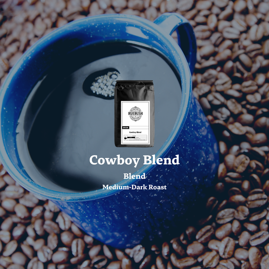 Blue enamel mug with a coffee bag labeled Cowboy Blend on a background of coffee beans